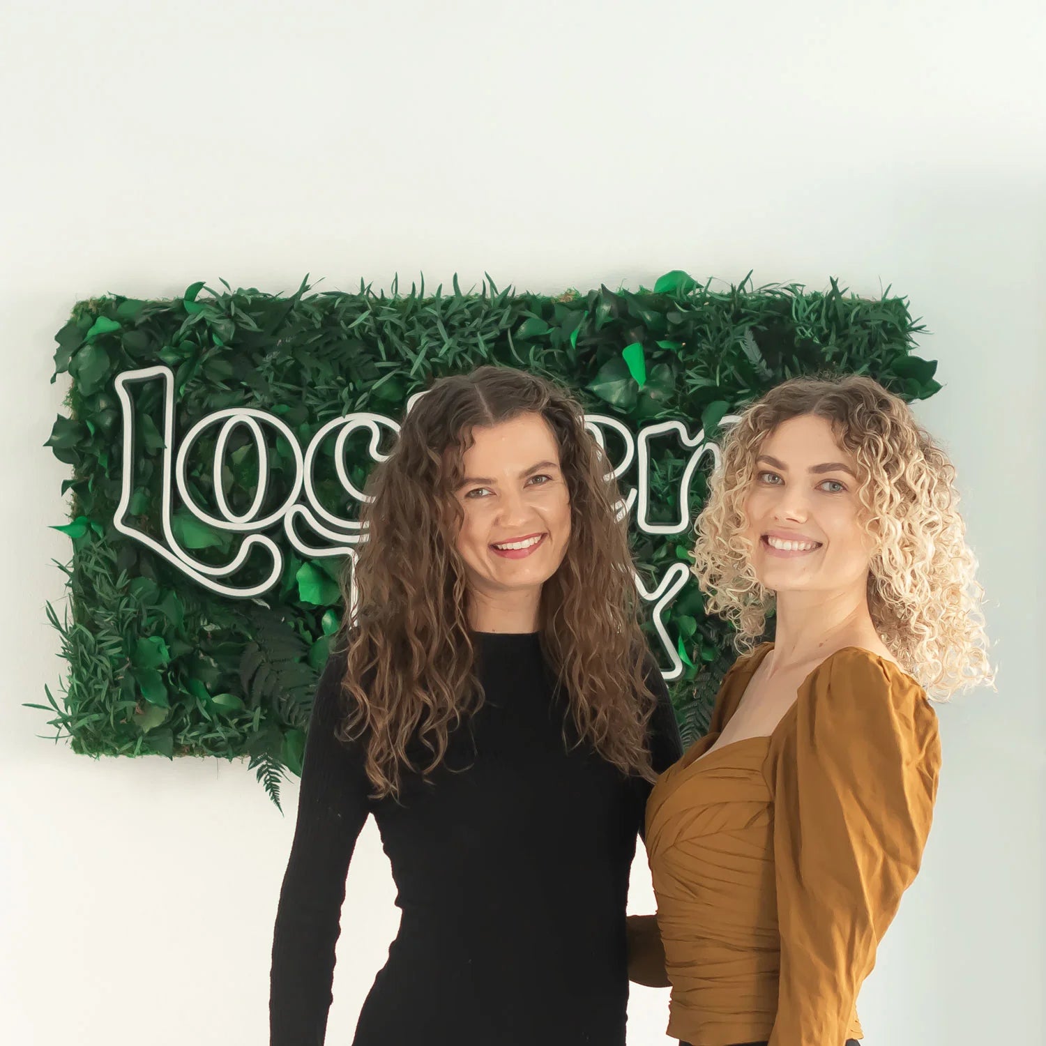 Die zwei Gründerinnen von Lockenbox mit lockigem Haar vor grünem Lockenbox-Logo.